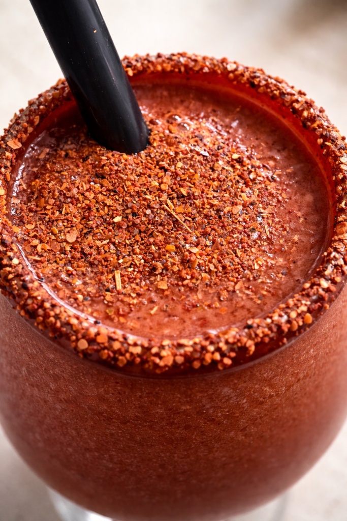 Primer plano de un frappe diablito de chabacano con pulpa de tamarindo y borde escarchado con chile.