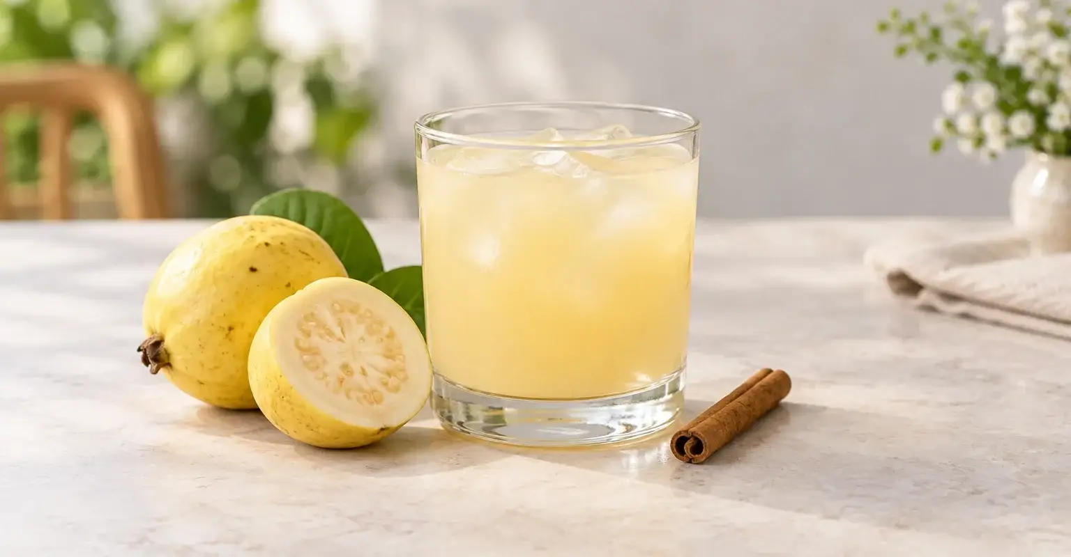 Infusión fría de guayaba con canela con el vaso completo junto a guayabas y canela